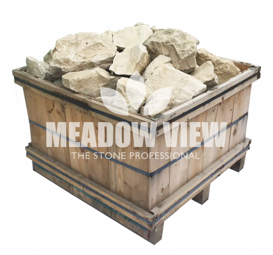 A wooden crate filled with large, irregular-shaped rocks. The crate has the words "Paving Shopper Cotswold Rockery - 250mm" printed on its side.