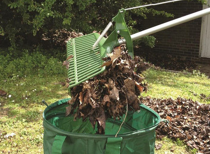 During the garden cleanup on a grassy area, the Paving Shopper Grabrake with its long handle effectively lifts dead leaves into a green outdoor bag.