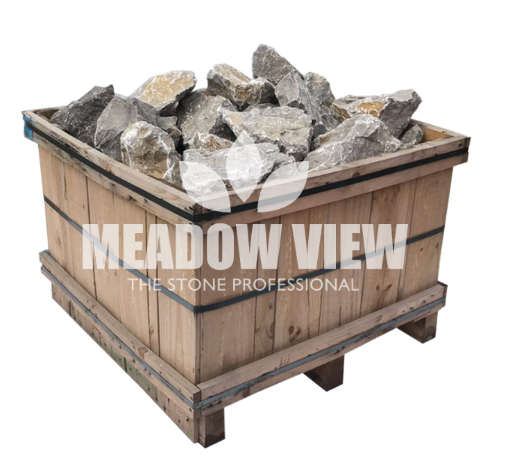 A wooden crate filled with large, rough stones, with the text "Paving Shopper - Longstone Rockery, 250mm" overlaid on the image.