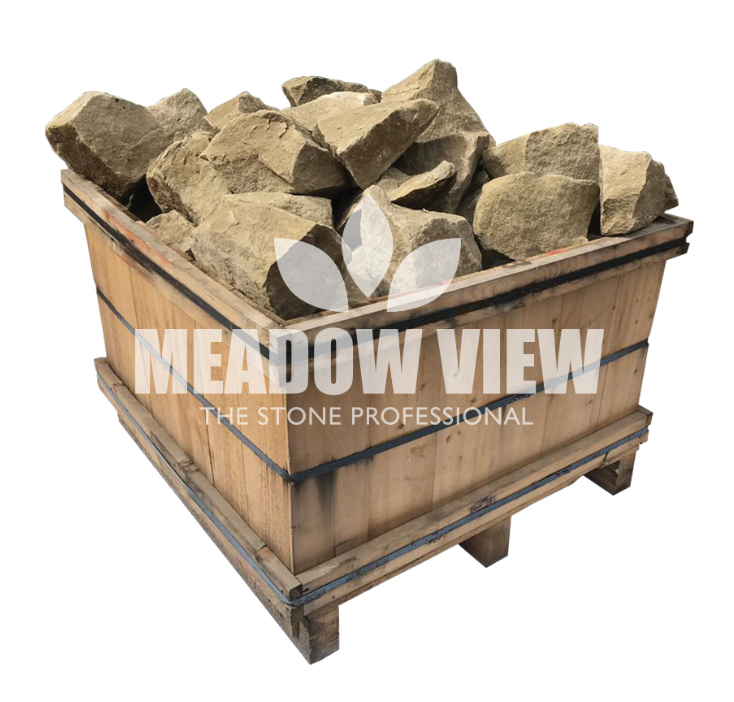 A wooden pallet crate is filled with large, uncut brown stones. The crate has the text "Paving Shopper Lumbshill Rockery - 250mm" and a leaf logo printed on its side.