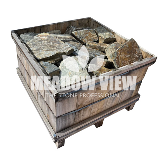 A wooden crate filled with large, rugged stones labeled "Paving Shopper - Rustic Slate Rockery - 250mm.