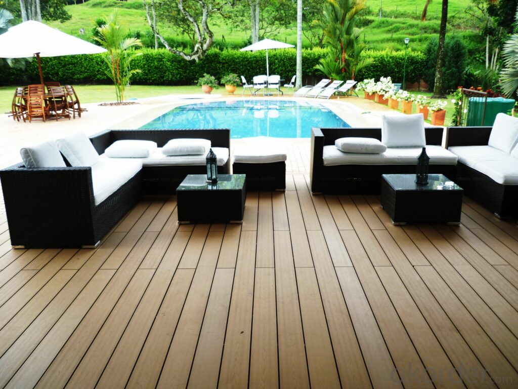 The outdoor patio showcases Paving Shopper's Composite Decking in Wild Field Brown, measuring 58.24m², alongside wicker sofas and a coffee table with a durable wood grain finish, all set beside a swimming pool surrounded by lush greenery.